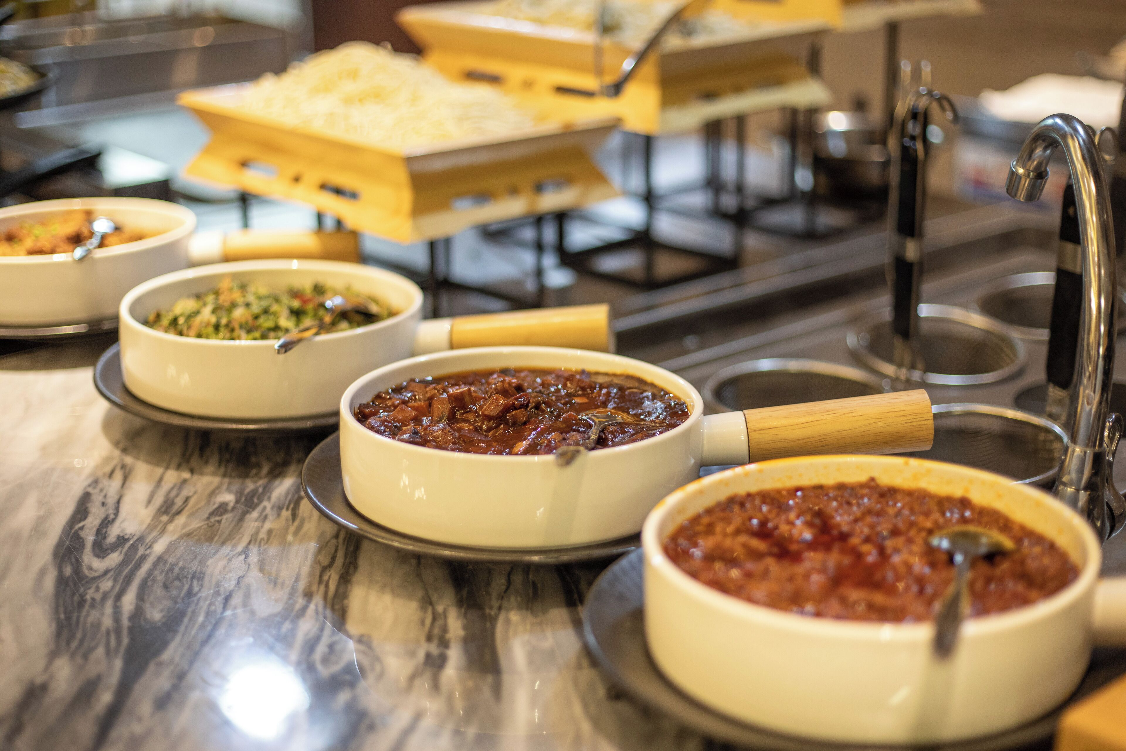 A buffet with various dishes in white bowls, a sink, and a faucet.