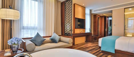 A hotel room with a large bathtub, a sofa with cushions, a TV, and a decorative screen.