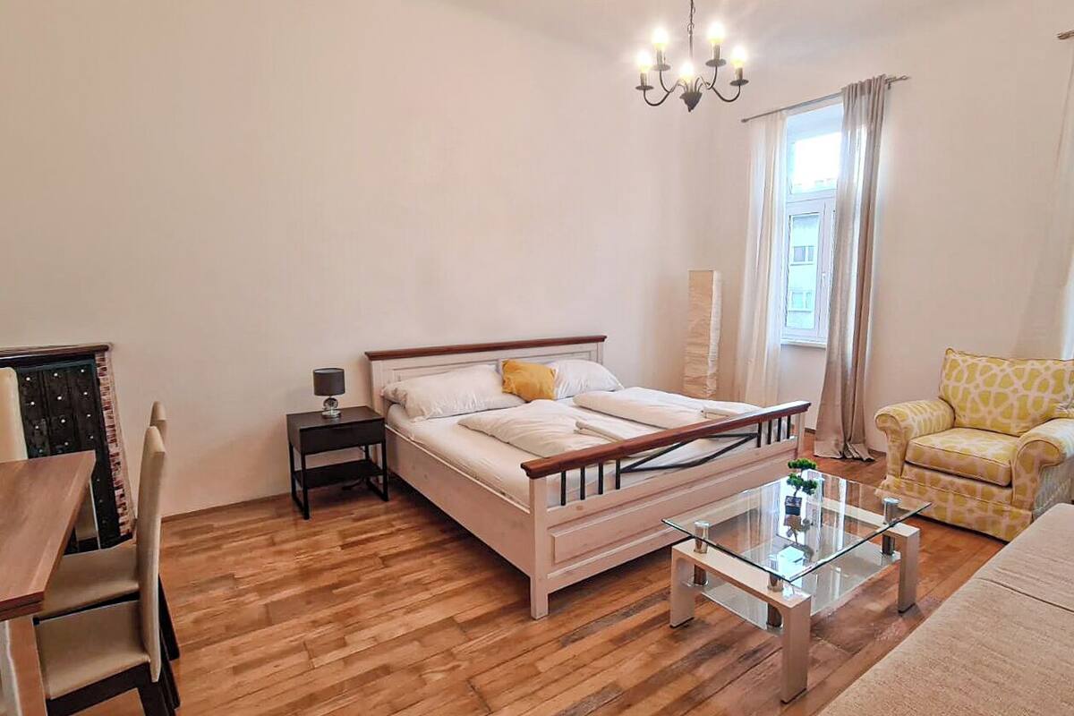 A bedroom with a bed, bedside table, lamp, chair, and a small table with a plant.