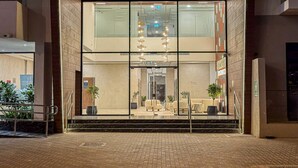 Een hotelentree met een glazen gevel, een trap die naar de lobby leidt en een modern interieur met zitplaatsen en planten.
