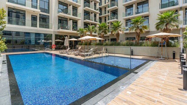 Een modern hotel met een groot buitenzwembad, ligbedden en palmbomen.