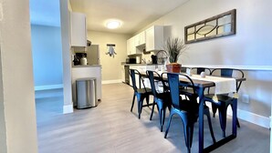 Une cuisine moderne avec des meubles blancs, un coin repas comprenant une table et des chaises, et une poubelle.