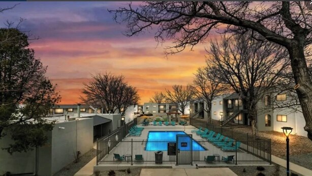 Un espace piscine offrant une vue sur le coucher de soleil, entouré d’immeubles et d’arbres.