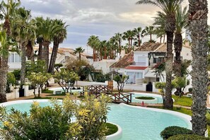 A resort with a swimming pool, palm trees, and white buildings with red-tiled roofs. - Studio bungalow in Roquetas (Roquetas de Mar)