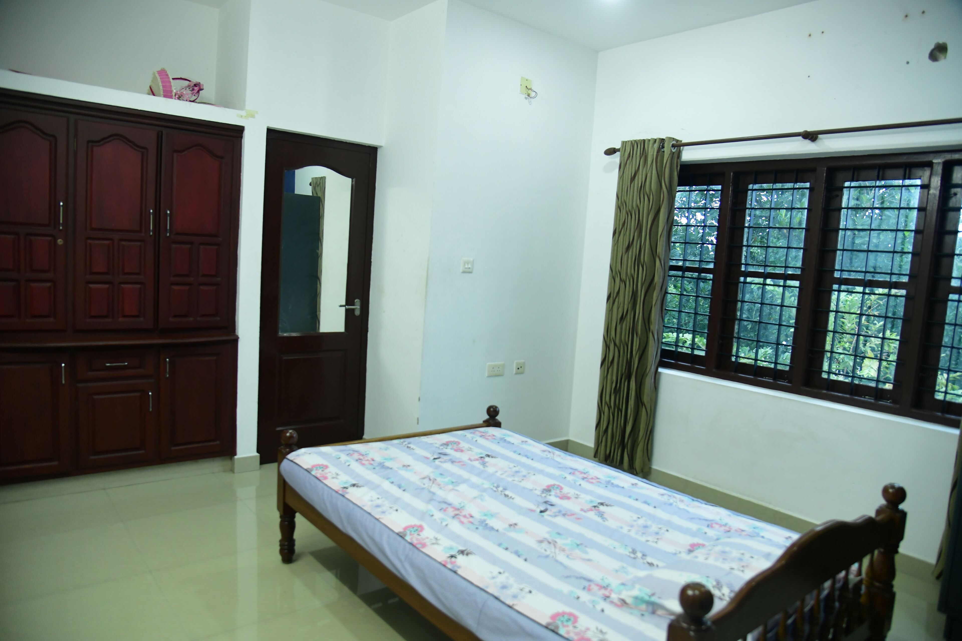A bedroom with a single bed, a wardrobe, a mirror, and a window with curtains.