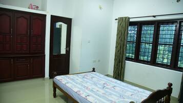 A bedroom with a single bed, a wardrobe, a mirror, and a window with curtains.