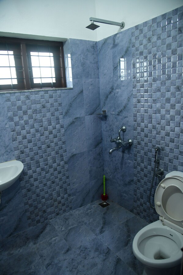 Un baño con piso de baldosas, inodoro, lavamanos y zona de ducha.