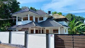Una casa a due piani con facciata bianca, tetto scuro e ingresso chiuso da cancello.
