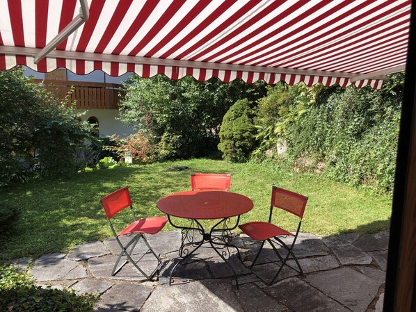 Un patio con un toldo a rayas rojas y blancas, una mesa redonda y cuatro sillas rojas.