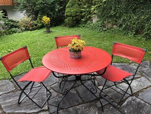 Una mesa redonda con cuatro sillas rojas, un jarrón con flores amarillas y un patio empedrado con piedra.