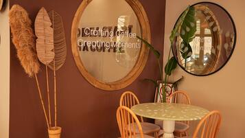 Un comedor con una mesa redonda, sillas de mimbre, un espejo y plantas decorativas.
