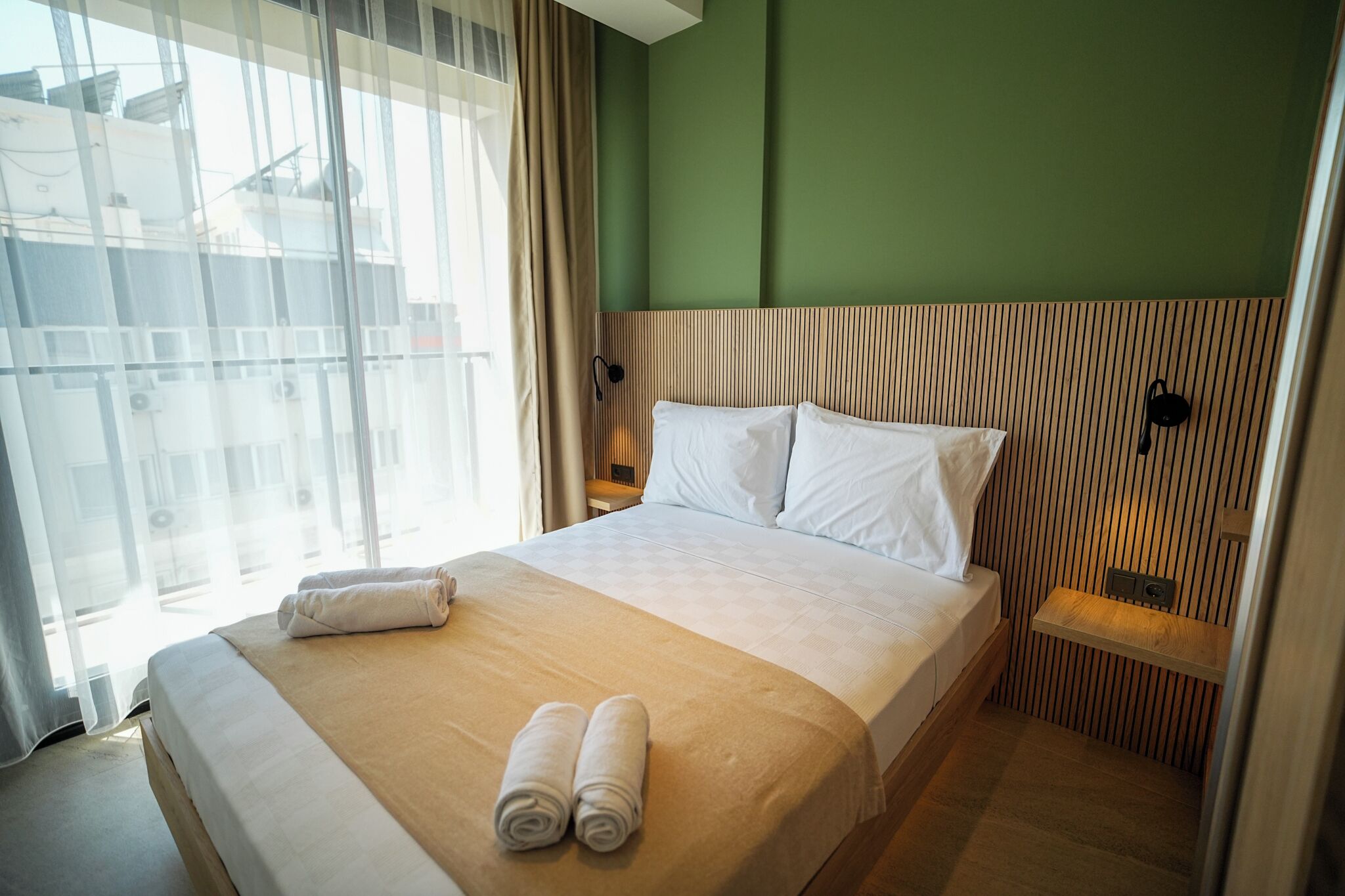 A hotel room with a large bed, a bedside table, a nightstand, and a view of the outside.