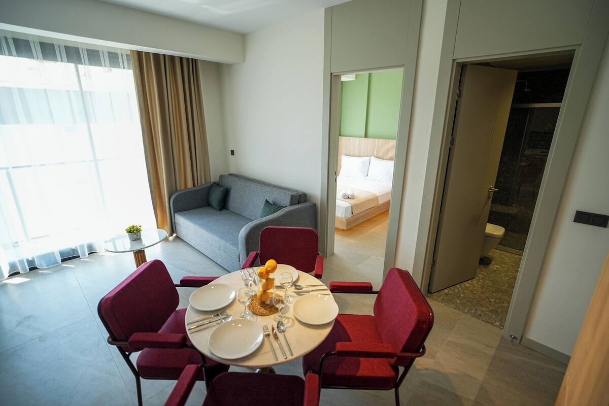 Una camera d'albergo con zona pranzo, divano e bagno parzialmente visibile attraverso una porta aperta.