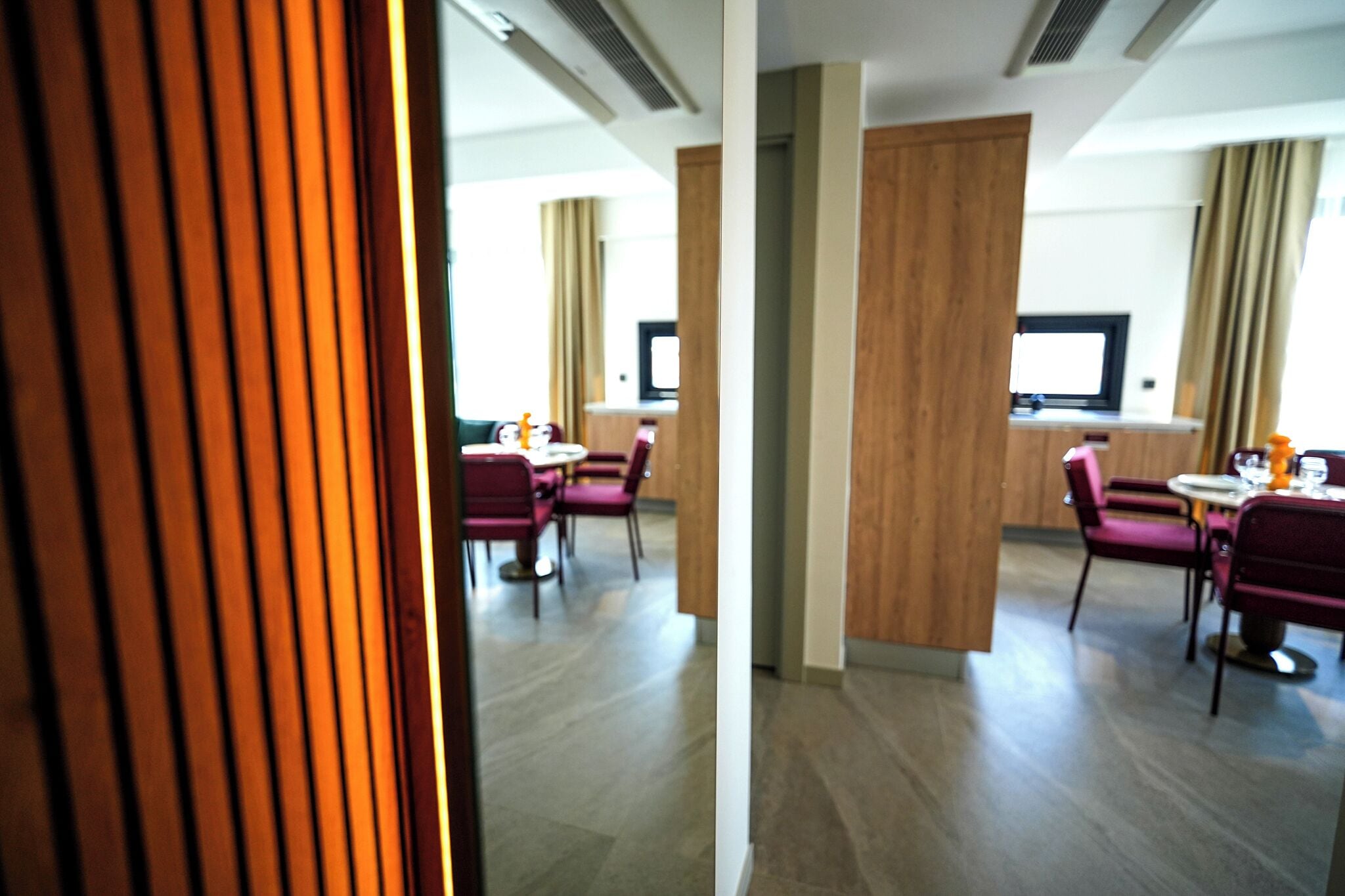 Habitación de hotel con diseño moderno, que incluye una pared decorativa de madera, un televisor de pantalla plana y una zona de comedor con sillas rojas y una mesa.