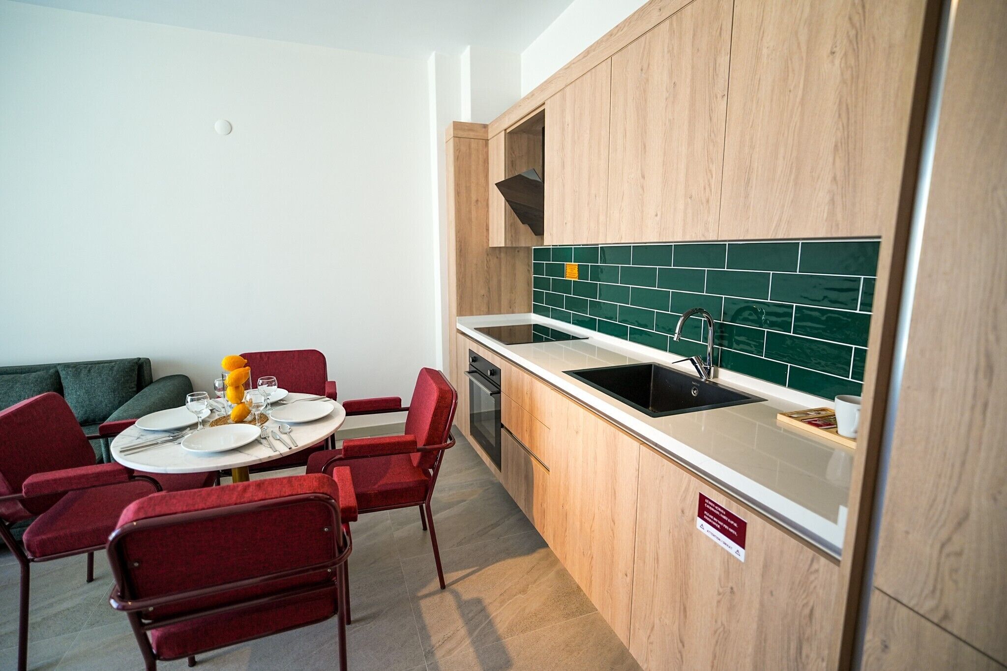 A compact kitchen with a sink, stove, and a dining area with red chairs and a table set for two.