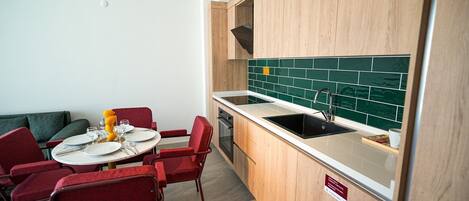 A compact kitchen with a sink, stove, and a dining area with red chairs and a table set for two.
