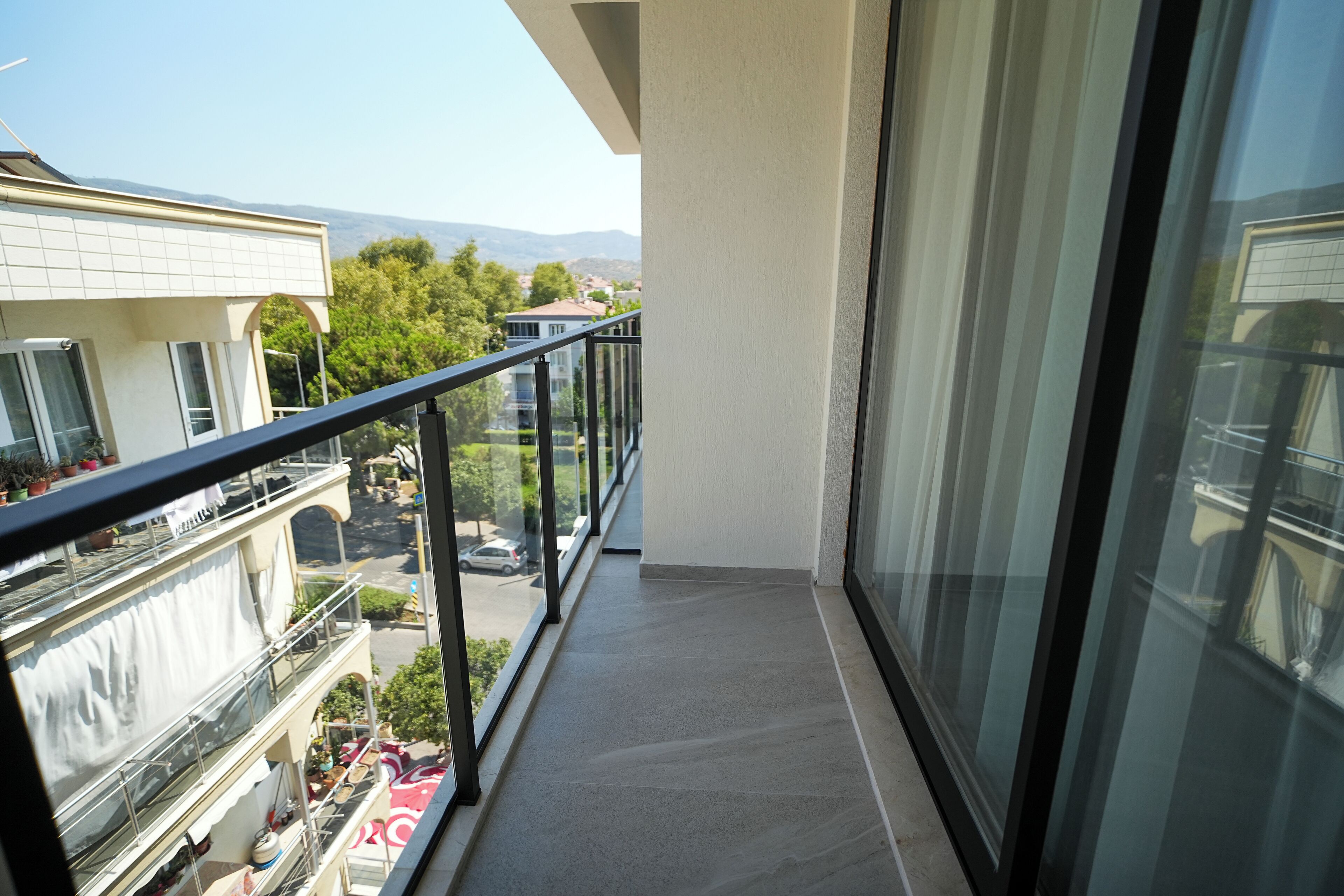 A balcony with a glass railing, overlooking a street with parked cars and buildings.