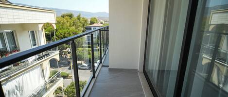 A balcony with a glass railing, overlooking a street with parked cars and buildings.