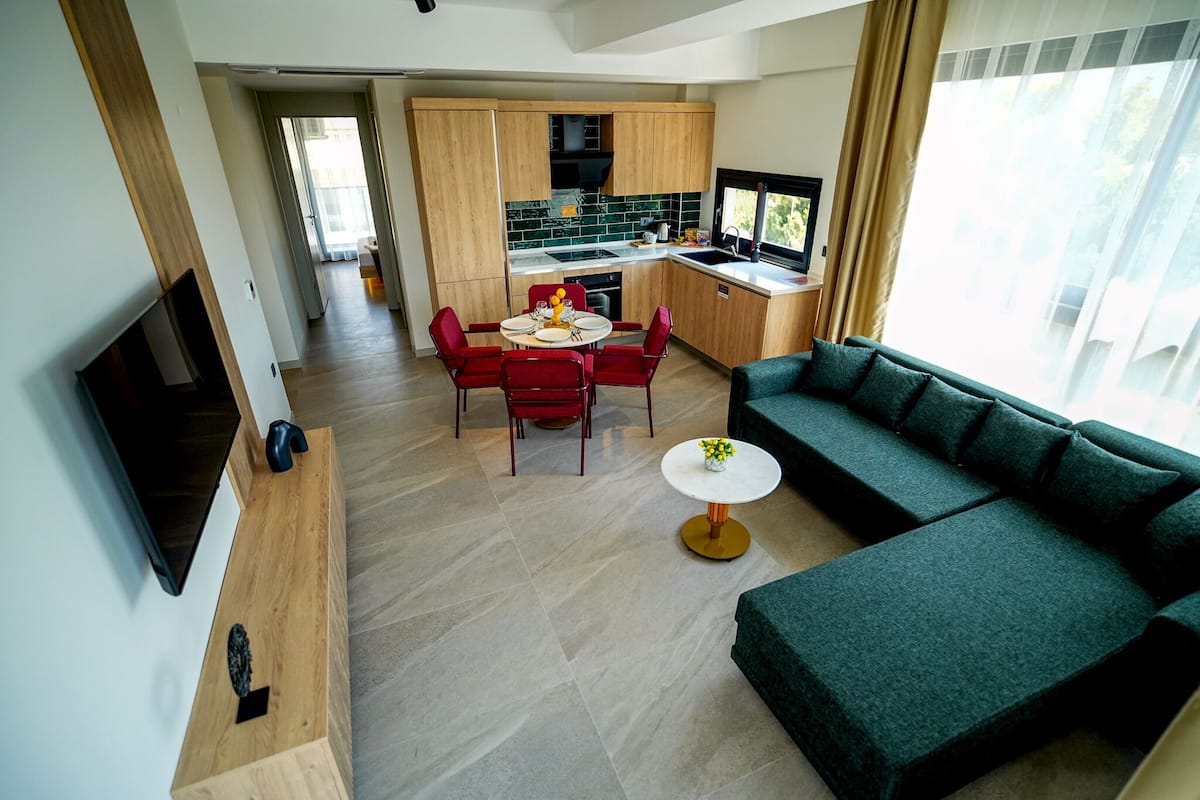 Un soggiorno moderno con un divano verde, un tavolo da pranzo con sedie rosse e un angolo cucina con mobili in legno e una televisione.