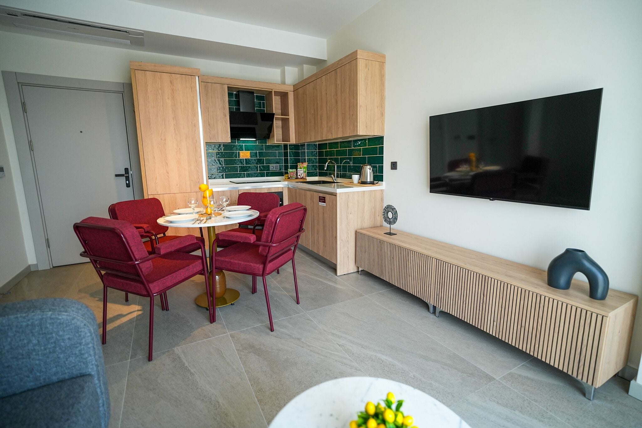 Una cocina moderna con armarios de madera, un comedor con sillas rojas, un televisor en la pared y un radiador debajo.