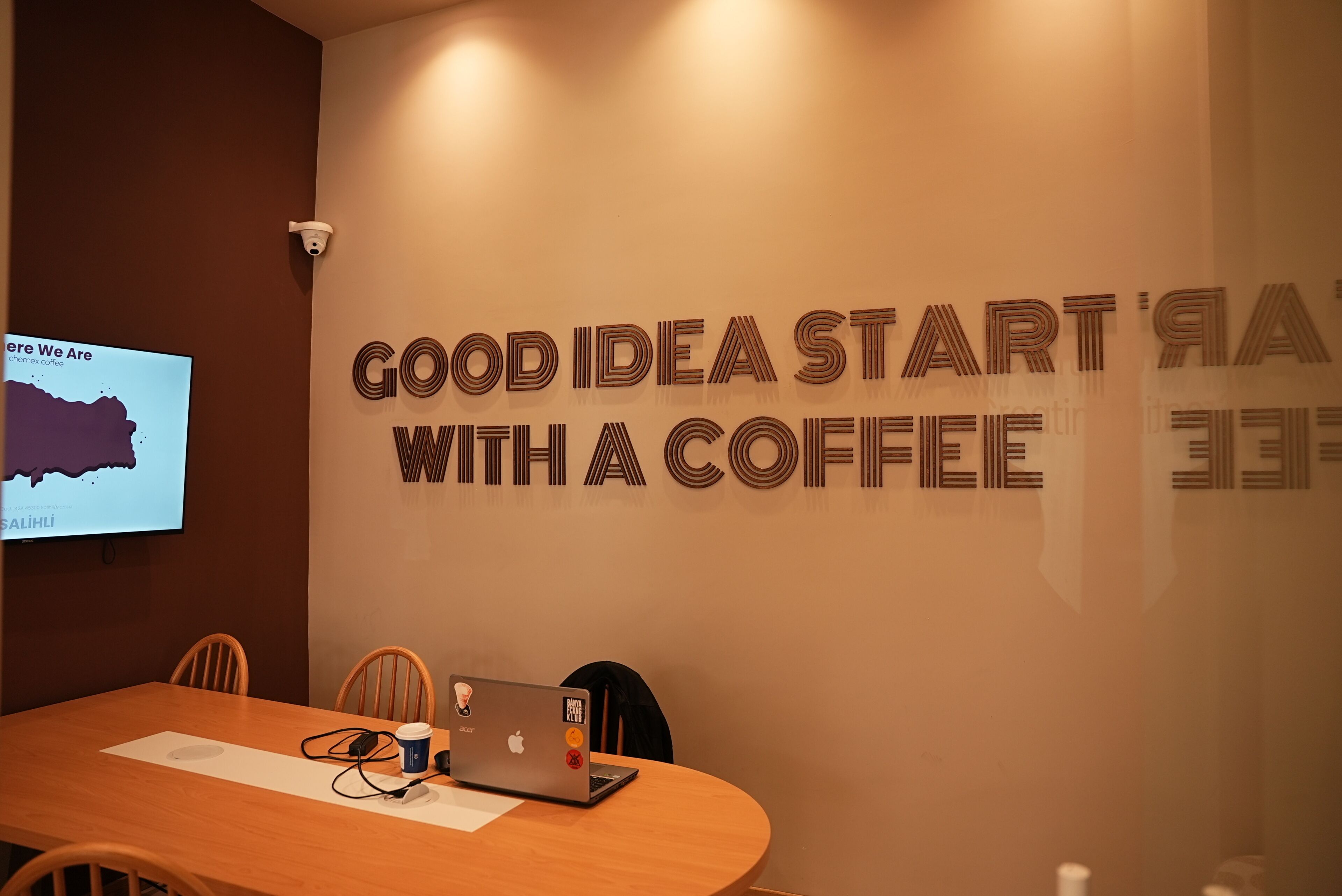 A conference room with a wooden table, chairs, a laptop, and a coffee cup. A screen displays a map and text.