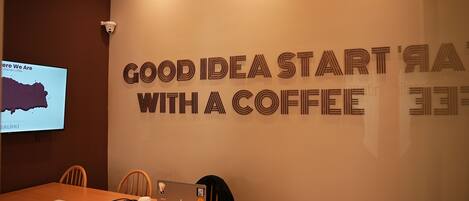 A conference room with a wooden table, chairs, a laptop, and a coffee cup. A screen displays a map and text.