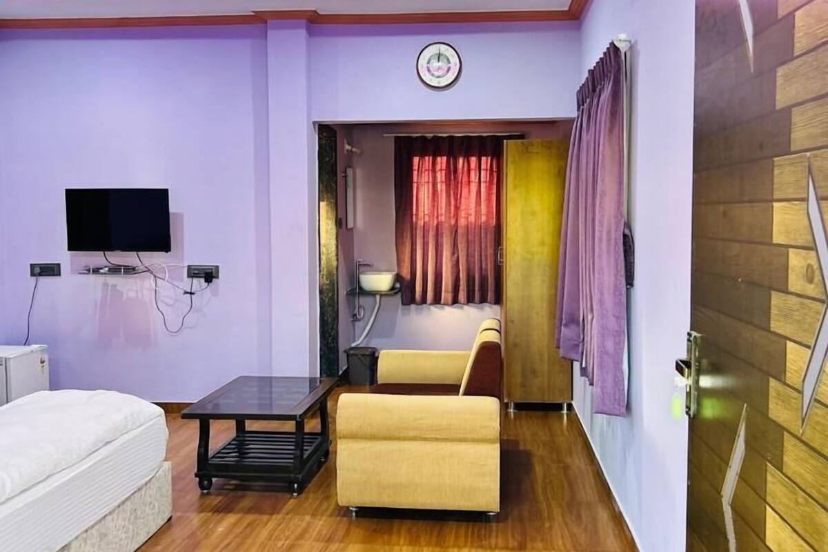 A modern living room with a sofa, a coffee table, a flat-screen TV mounted on the wall, and an air conditioning unit.