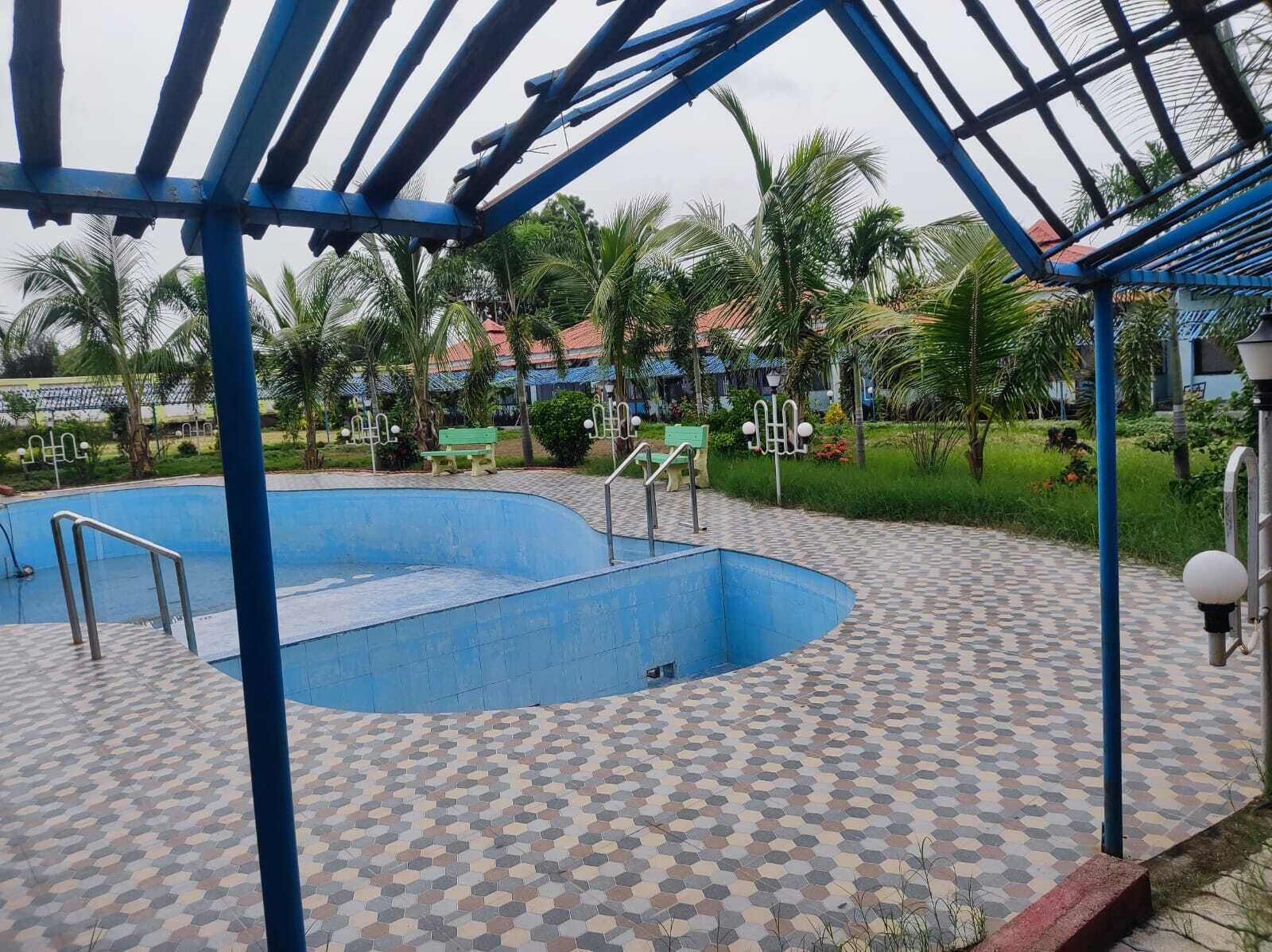 Una piscina con borde de azulejos azules, rodeada de palmeras y una zona cubierta con vigas azules.