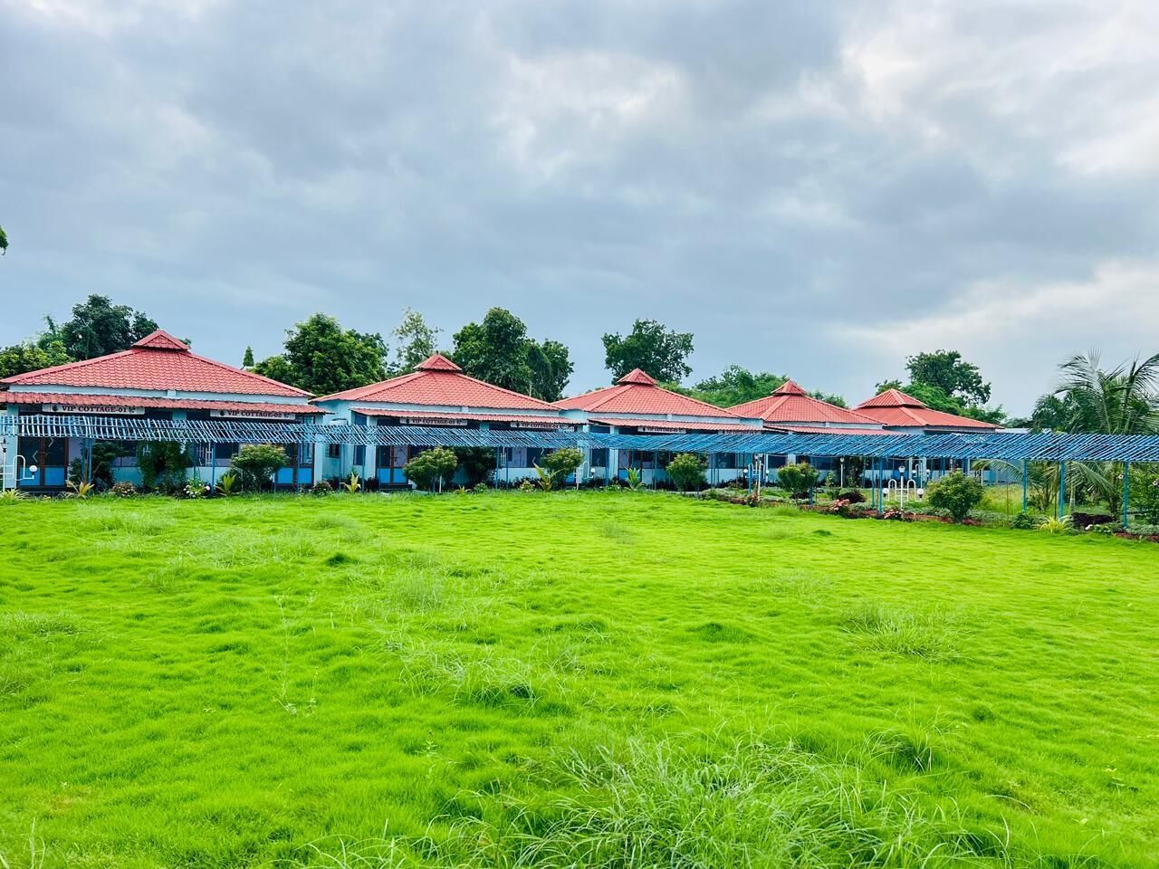 Una hilera de edificios con tejados rojos y toldos azules, rodeados por un campo verde.