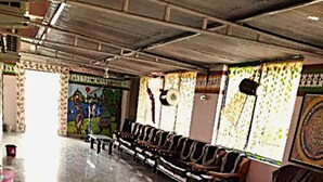 A spacious hall with rows of seating, a central table, and a mural on the wall. - Vrundavan Village Resort and Home Stay (Garudeshwar)