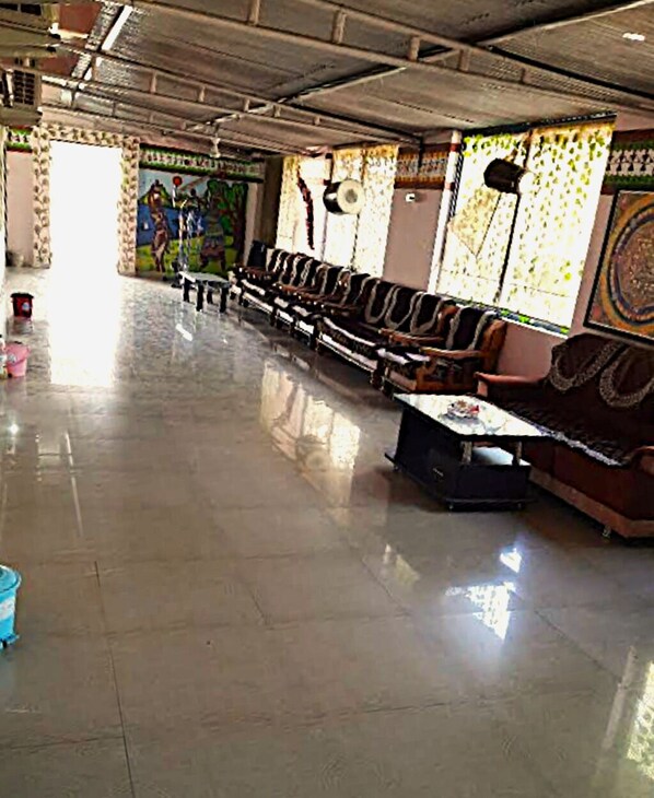 A spacious hall with rows of seating, a central table, and a mural on the wall. - Vrundavan Village Resort and Home Stay (Garudeshwar)