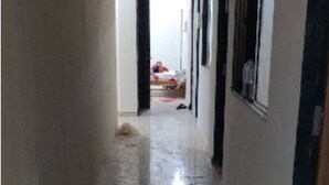A narrow, dimly lit hallway with a tiled floor, leading to a room with a bed and a person sitting on it. - Vrundavan Village Resort and Home Stay (Garudeshwar)