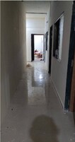 A narrow, dimly lit hallway with a tiled floor, leading to a room with a bed and a person sitting on it.
