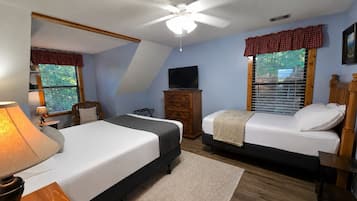 Een slaapkamer met twee bedden, een plafondventilator, een televisie op een houten dressoir en ramen met zonwering.