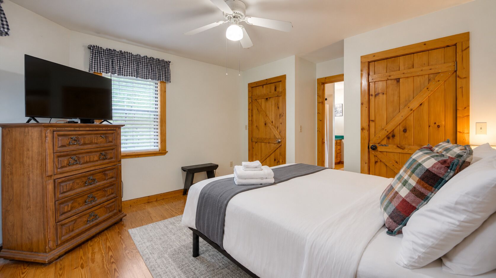A bedroom with a bed, wooden dresser, television, and a ceiling fan.