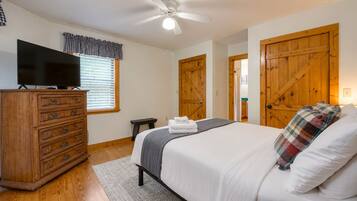 A bedroom with a bed, wooden dresser, television, and a ceiling fan.