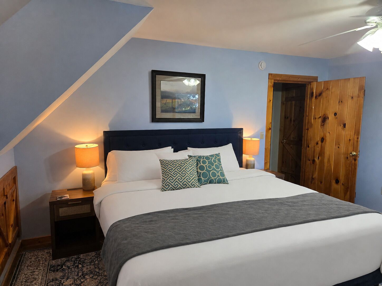 Une chambre à coucher avec un lit, deux lampes de chevet, un tableau encadré au mur et une porte en bois.