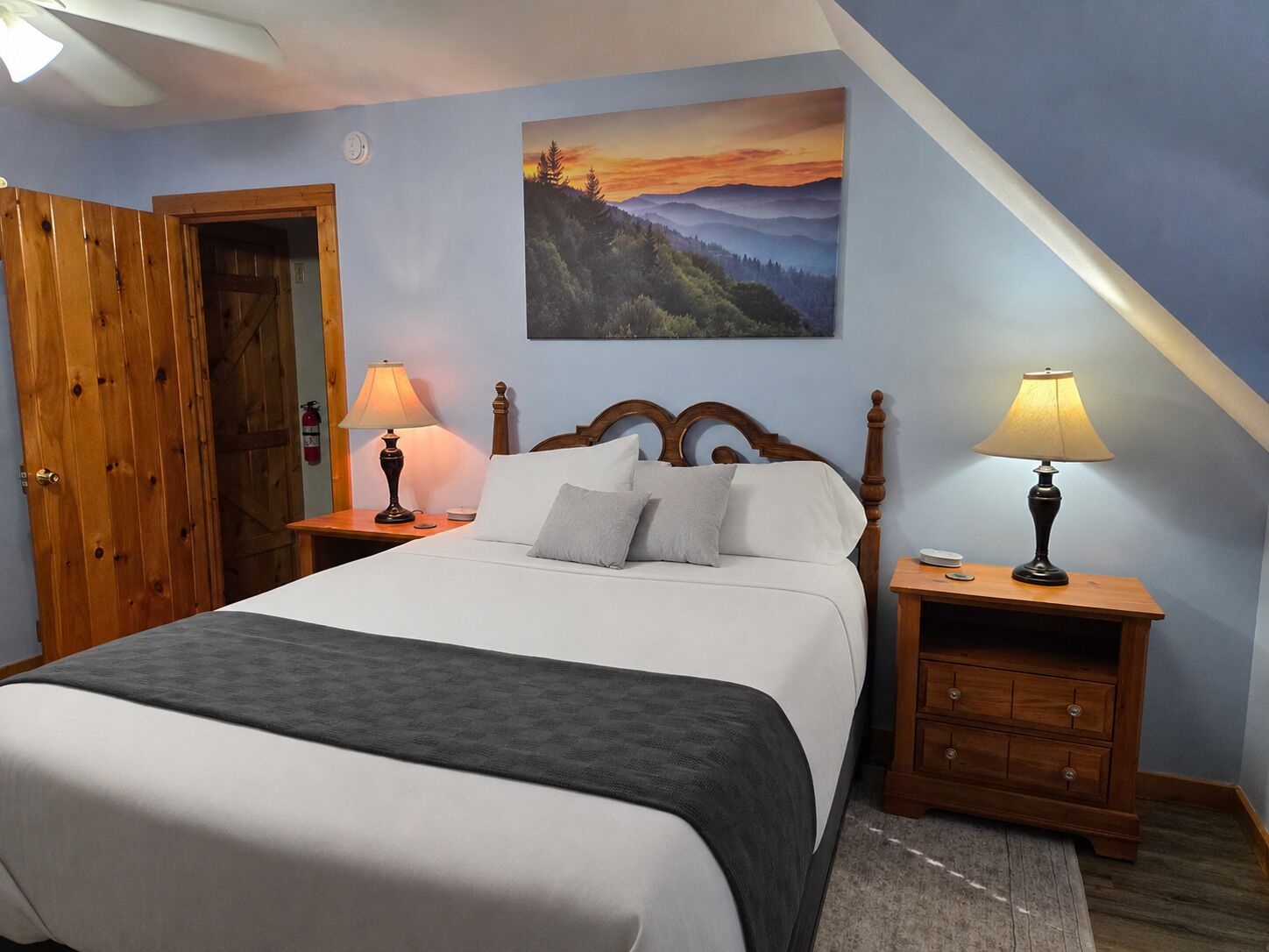 Un dormitorio con una cama, dos mesitas de noche, una puerta de madera y un cuadro en la pared.
