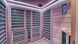 Uma sala de sauna com paredes de madeira, teto com sistema de ventilação e um painel digital exibindo temperatura e cronômetro.