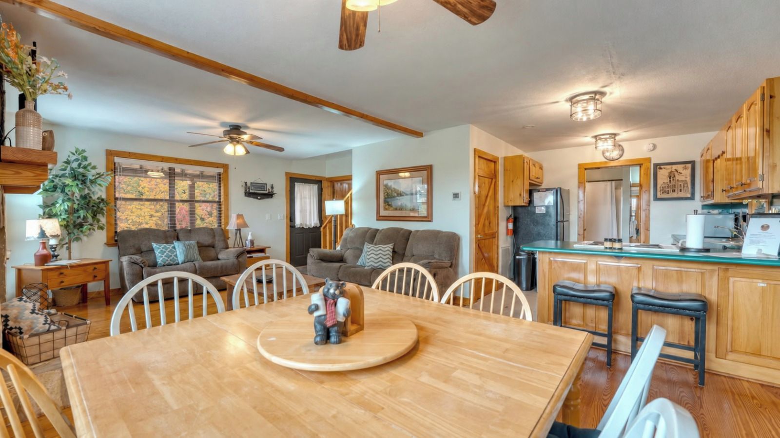 A cozy living room with a dining table, sofas, and a kitchen area with wooden cabinets and a refrigerator.