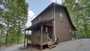 A wooden cabin with a porch, surrounded by trees.