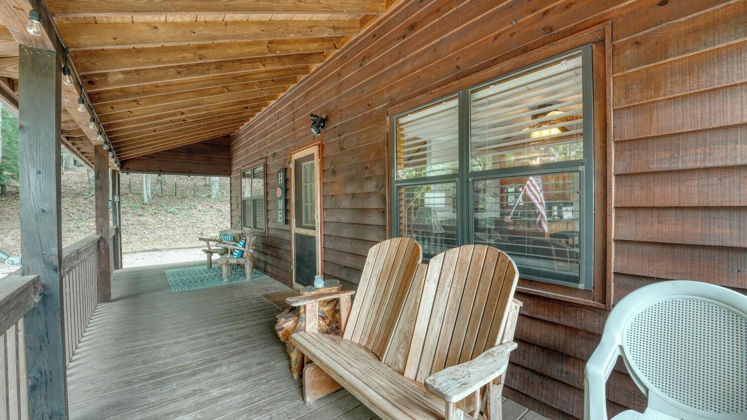 A wooden cabin with a porch, two Adirondack chairs, and a table.