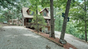 A cabin with a gravel driveway, surrounded by trees.