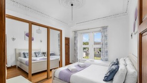 Un dormitorio con dos camas, piso de madera, ventana con cortinas e iluminación en el techo.