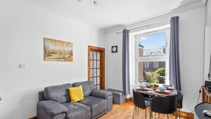 Una sala de estar moderna con un sofá gris, una mesa de comedor con sillas, una ventana con cortinas y un cuadro en la pared.