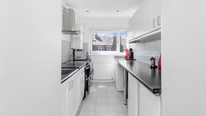 Una cocina moderna con armarios blancos, una encimera negra y vistas a una casa a través de una ventana.