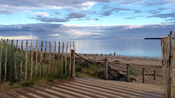 Una pasarela de madera que conduce a una playa arenosa, con una cerca de madera y una barrera de cuerda.