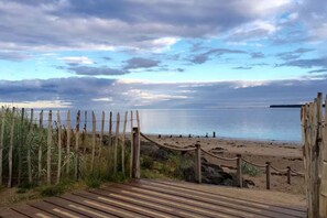 A wooden boardwalk leading to a sandy beach with a wooden fence and rope barrier.
