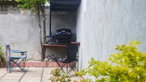Un espace extérieur aménagé avec un barbecue, une chaise pliante et une petite table.