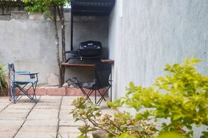 Een terras met een barbecue, een opklapbare stoel en een klein tafeltje.